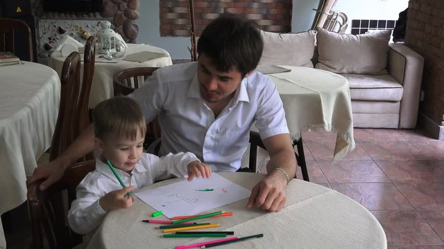 young father with his son draws pencils sitting in a cafe when there is no customer