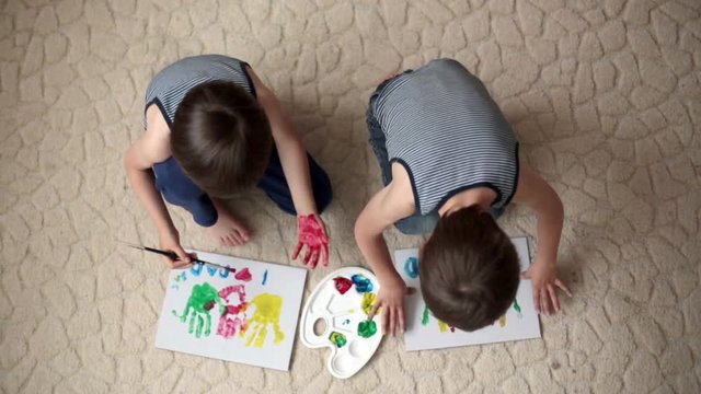 Two adorable boys, preparing fathers day gift for dad,  painting with hands on a carton at home