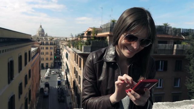 Young, happy woman using smartphone while sitting on the ledge with city view, 120fps
