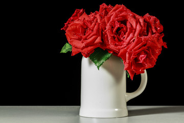 Bouquet of red roses into a white ceramic mug, on black background