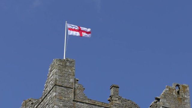 English St George cross flag waving in the wind above castle with blue sky background