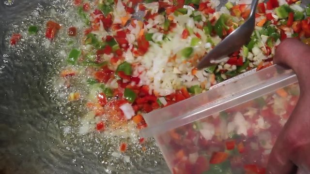 Cocinando una Paella - Echando cebolla y pimiento a la paella con aceite hirviendo

