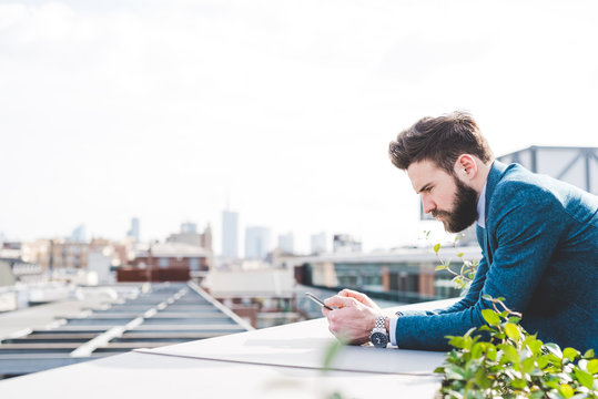 Young businessman reading smartphone text on office roof terrace