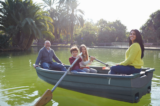 Family in rowing boat on lake looking at camera smiling
