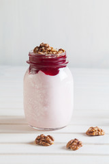 Homemade yogurt with jam and walnuts in a jar on a white wooden