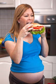 Hungry pregnant woman eatinga big burger,junk food.