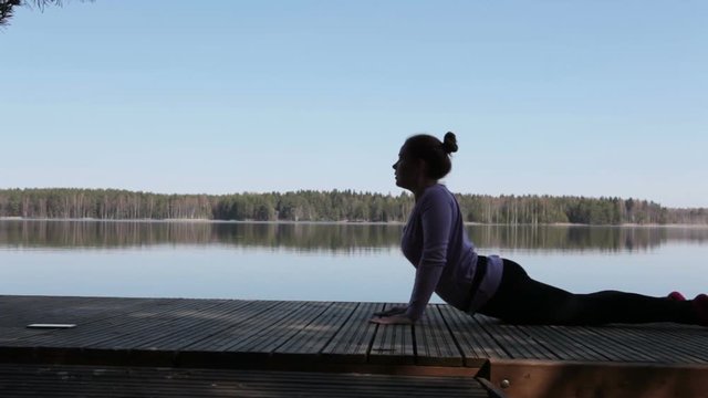 Making exercices on wooden pier on lake shore
