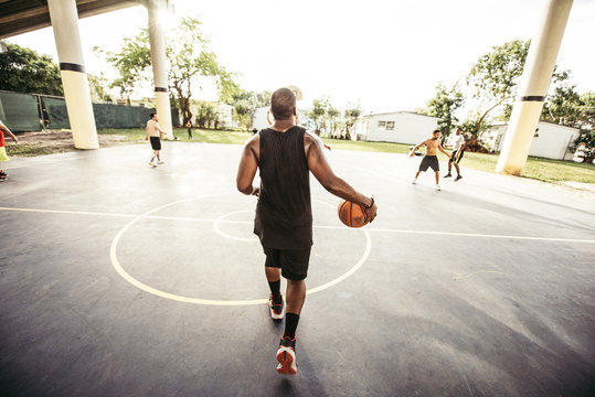 Full length rear view of young man walking on basketball court holding basketball