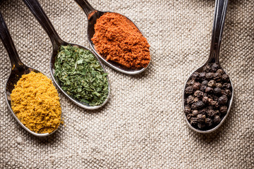 Spices on old metal spoons. Linen fabric background.