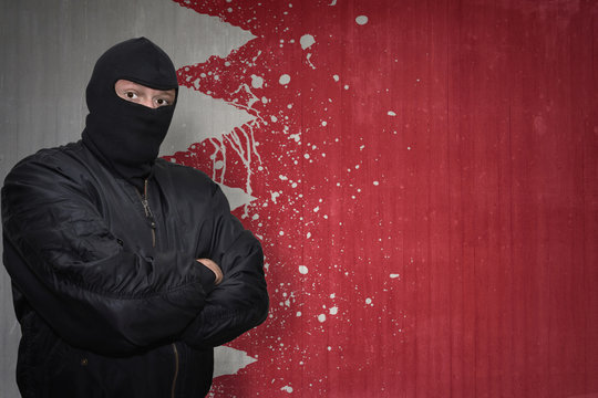 dangerous man in a mask standing near a wall with painted national flag of bahrain