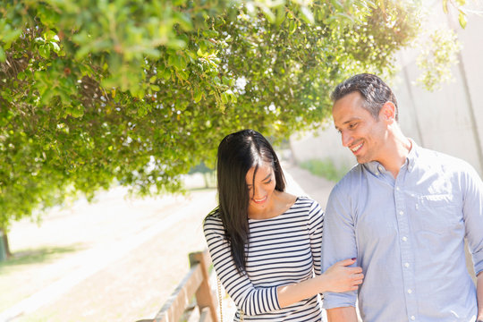 Couple underneath tree linking arms smiling