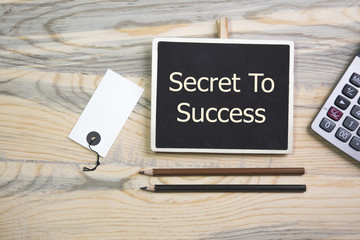 sentence secret to success written with chalk on a blackboard, on a table with pen, calculator