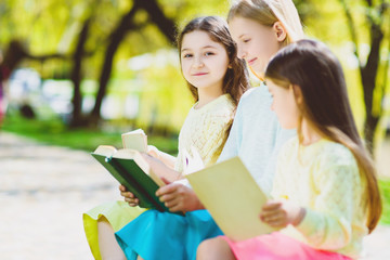 Fototapeta premium Children reading books at park. Girls sitting against trees and lake outdoor