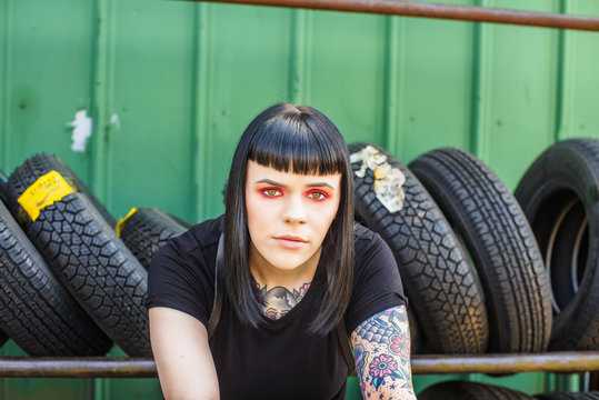Tattooed woman in front of tyres looking at camera
