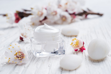 Facial cream with beauty cherry blossoms and white pebblestone on wooden background