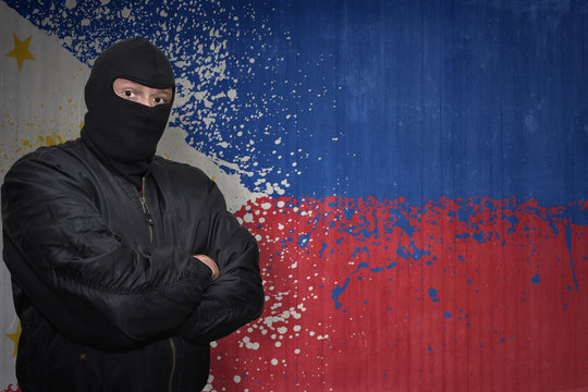 dangerous man in a mask standing near a wall with painted national flag of philippines