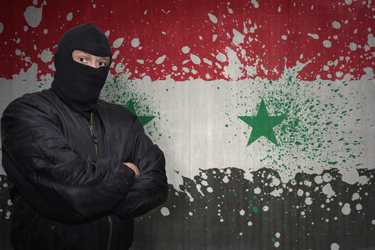 dangerous man in a mask standing near a wall with painted national flag of syria
