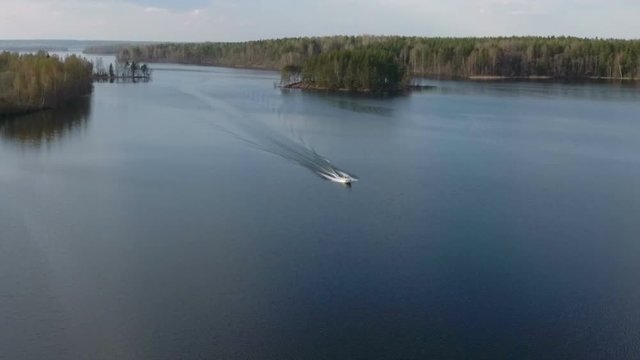 Slow motion of speed boat driving on forest lake. Aerial view at the distance. Russia
