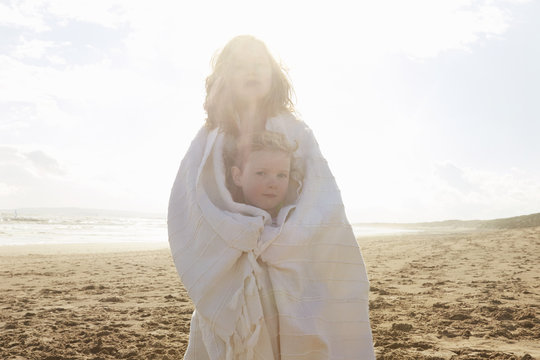 Portrait of two sisters wrapped in blanket on beach, Camber Sands, Kent, UK