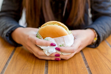 Girl holding a Burger. Teen girl with a delicious burger. Hand holding a tasty fast food cheeseburger. The concept of fast food. Tasty unhealthy Burger sandwich in hands, ready to eat