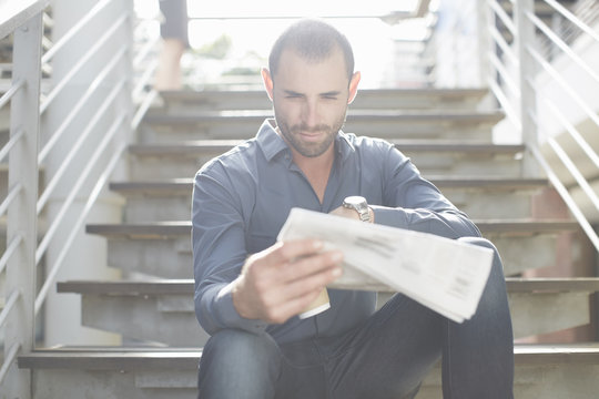 Businessman reading newspapers on staircase