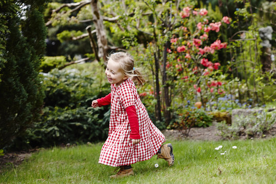 Young girl wearing gingham dress running in garden