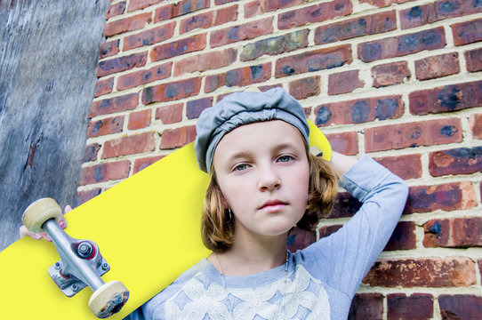 Portrait of sullen tomboy skateboarder girl leaning against brick wall