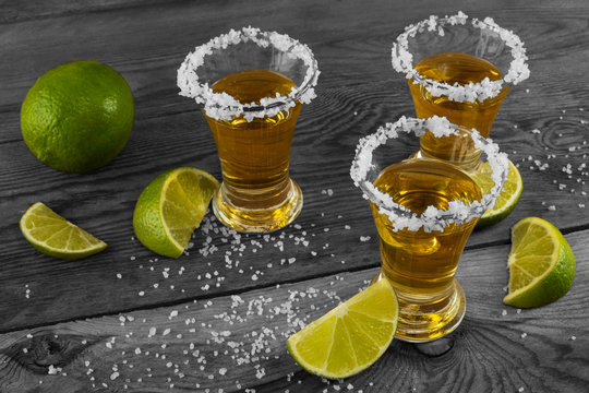 Three shots of gold tequila with lime and salt on the black background. Vintage toned photo. Tequila shot. Gold Mexican tequila. Tequila