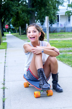 Portrait of girl sitting on skateboard on path