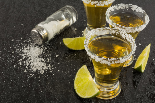 Gold tequila shots with lime on black background