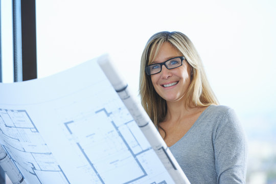 Portrait of mature female architect with plans in office