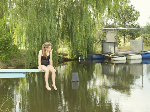 Teenage girl sitting on diving board over lake