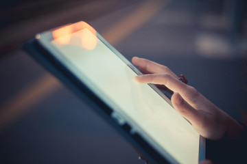 Hand of woman using digital tablet touchscreen at dusk