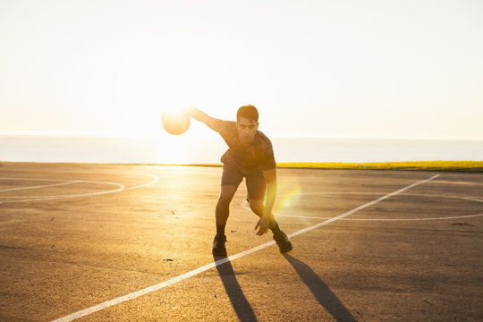 Young man, dribbling basketball on court, outdoors