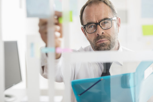 Businessman sticking adhesive notes to glass wall in office