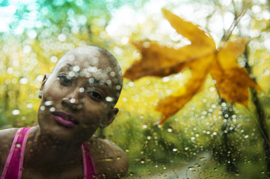 Portrait of young woman looking through rain covered window