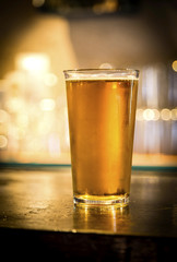 Glass of light beer on a dark pub.