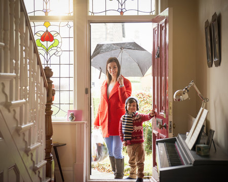 Mother and son arriving at front door of home on rainy day, portrait