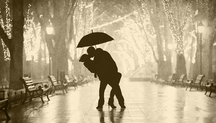 Couple with umbrella kissing at night alley.