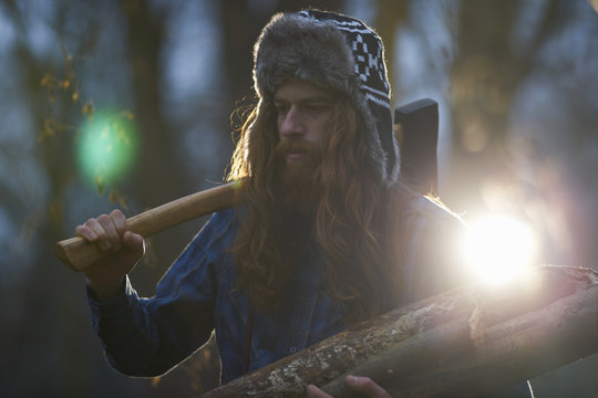Man in trapper hat chopping wood in countryside