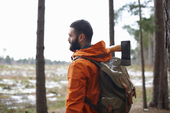 Young man carrying axe looking out from forest