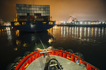 Tugboat manoeuvring cargo ship in harbor at night, Tacoma, Washington, USA