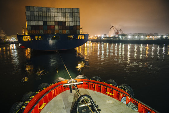 Tugboat manoeuvring cargo ship in harbor at night, Tacoma, Washington, USA