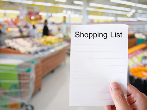 Female hand holding shopping list paper on grocery store blur ba