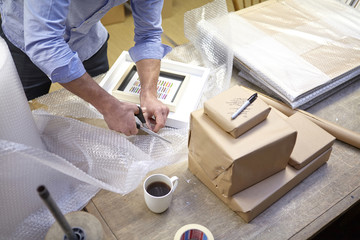 Man cutting bubble wrap on table in picture framers workshop