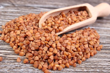 Heap of buckwheat groats with spoon on wooden surface