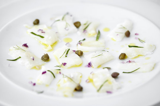 Close up of carpaccio of raw fish, capers and herbs on plate