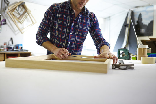 Mid adult man measuring frame on workbench in picture framers workshop
