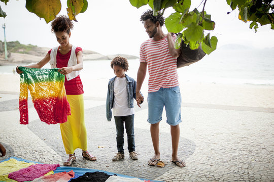 Couple and son choosing sweater from sidewalk stall, Ipanema beach, Rio De Janeiro, Brazil