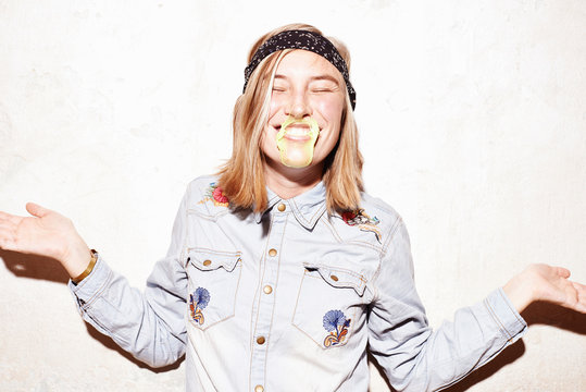 Studio shot of young woman with mouth covered in yellow gum bubble